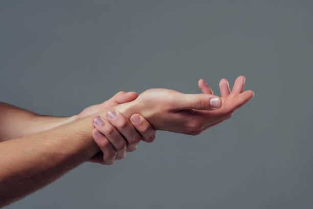 Man hand isolated on grey background. Close-up of man holding his wrist. Experiencing wrist pain.