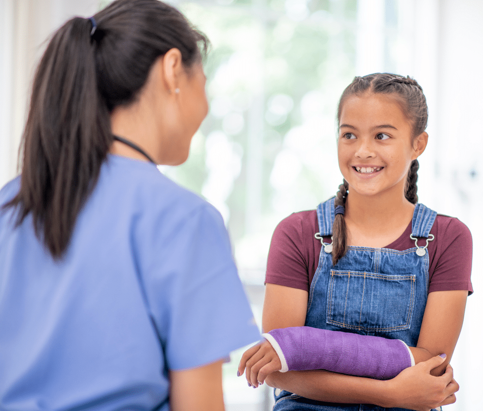 alt="Smiling young girl with a purple arm cast talking to a healthcare worker in blue scrubs."