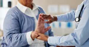 A physical therapist performs hand stretching exercises on a senior woman with arthritis during a physical therapy checkup.