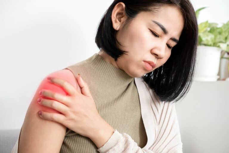 A woman is experiencing pain and stiffness in her shoulder due to frozen shoulder, and she is holding her shoulder for relief.