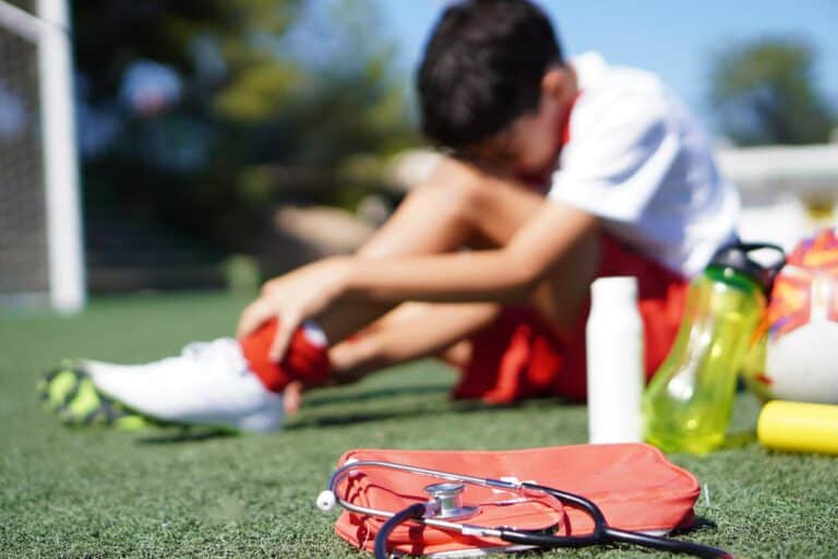 Faceless child injured during soccer game is sited on the grass with a sprained ankle.