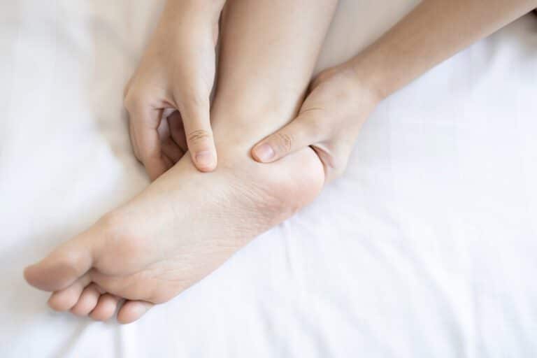 Hands of girl massage her foot in pain caused by tendinitis of the foot.