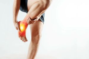 The man holds his hands to the ankle, the pain in his leg, the pain in the foot is highlighted in red. Light background. The concept of medicine, massage, physiotherapy, health.