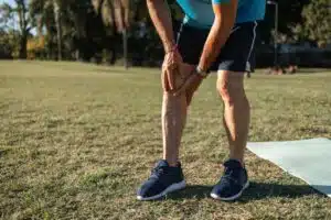 A man is experiencing knee pain while outdoors in an exercise area on a sunny day.