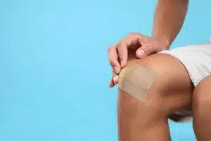 A man applying a bandage to his knee due to a torn ligament on a light blue background.