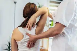 A teenage girl undergoes physical therapy to help relieve chronic back pain, guided by a therapist in a supportive setting.
